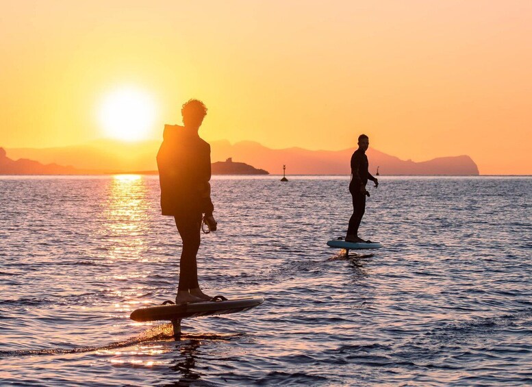 Two people paddleboarding on a calm sea at sunset with a distant landmass and a buoy. 5