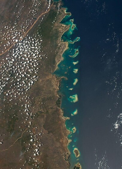 A coastal region with a dense cluster of white buildings on the left, a narrow strip of land, and a series of turquoise and green islands extending into the ocean. 5