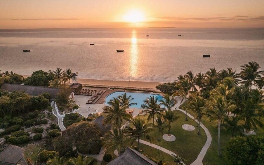A resort with a swimming pool, palm trees, and a sunset over the ocean. 2