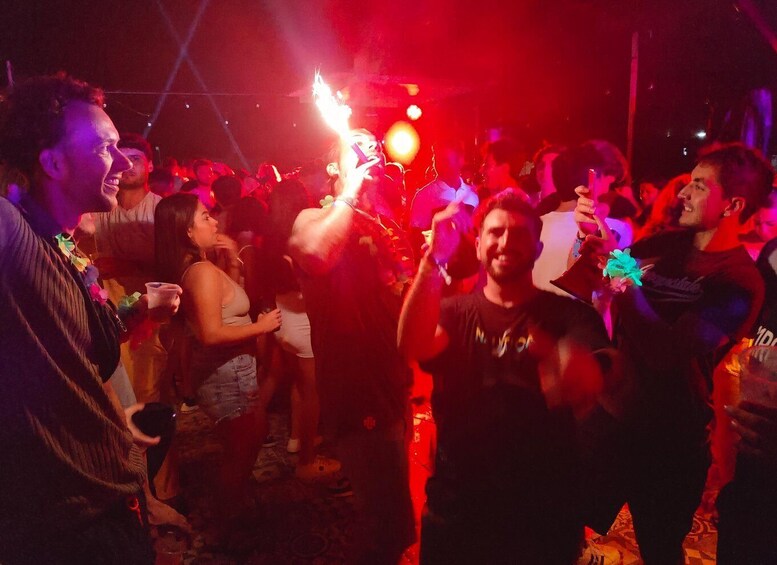 A crowded indoor event with people holding drinks and a person with a lit object. 3