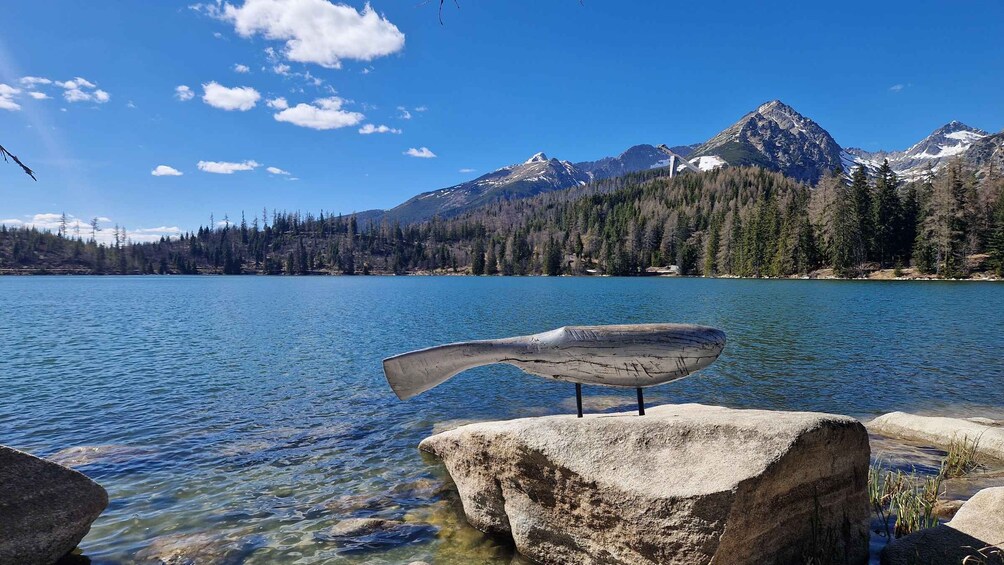 A clear lake with a wooden sculpture on a rock, surrounded by mountains and trees. 2