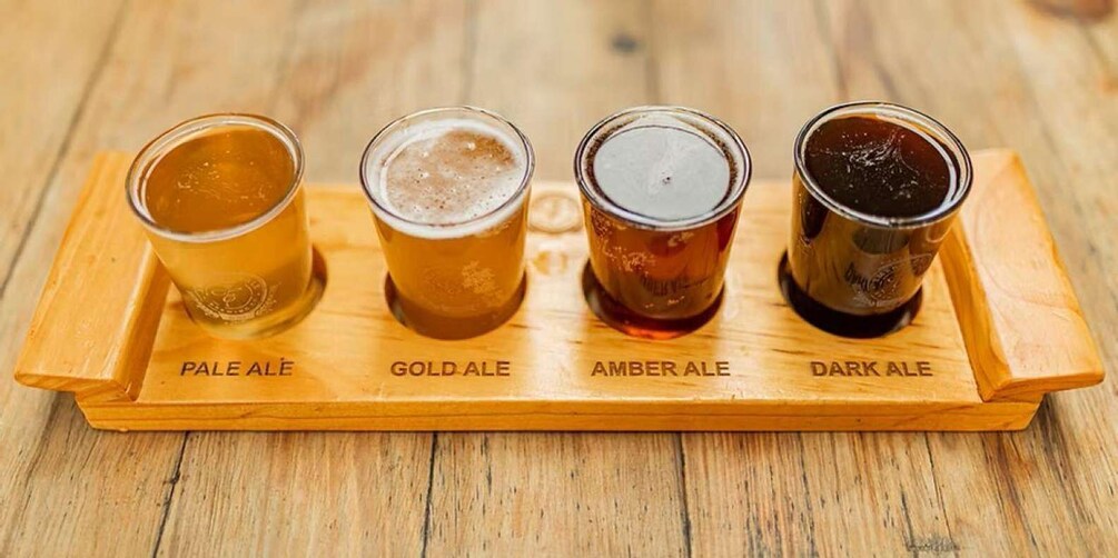 Four glasses of beer on a wooden tray labeled with their types: Pale Ale, Gold Ale, Amber Ale, and Dark Ale. 5