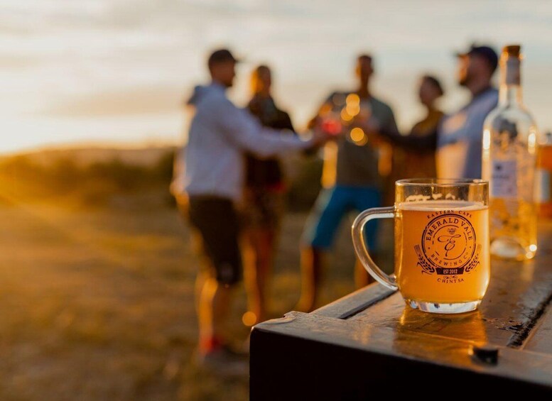 A group of people standing outdoors at sunset, with a beer mug on a table in the foreground. 1