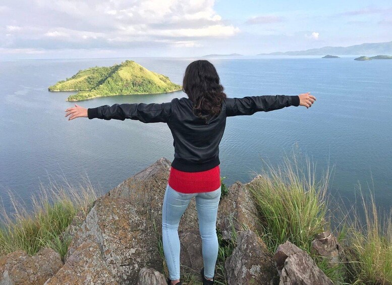 A person standing on a rocky outcrop with arms outstretched, overlooking a calm body of water and a small island. 3