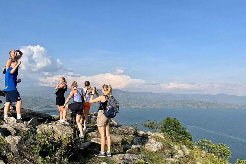 A group of people standing on rocky terrain overlooking a body of water with mountains in the distance. 1