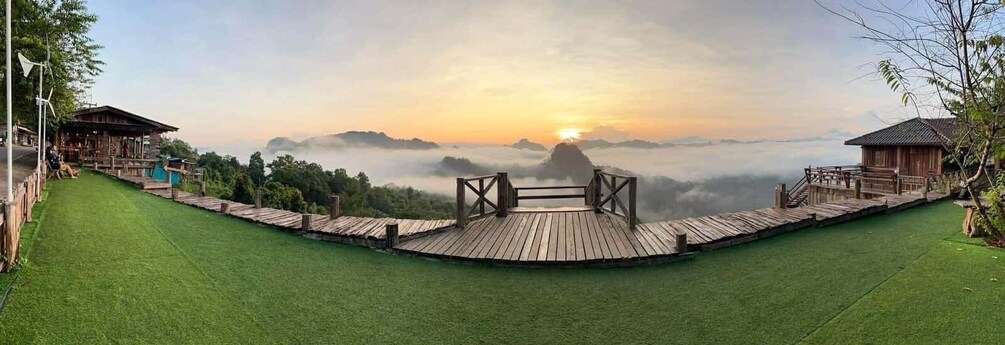 A wooden deck overlooking a lush green landscape with a sunrise or sunset in the background. 4