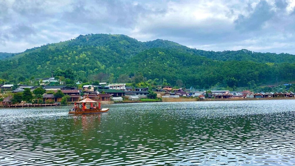 A river with a boat, a village, and a forested hill in the background. 1