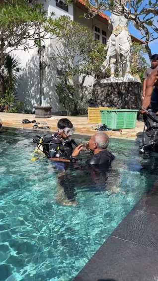 A pool with clear water, a statue, and a person in a wetsuit. 2