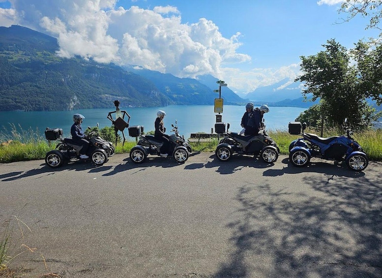 Four quad bikes parked on a road with a lake and mountains in the background. 1