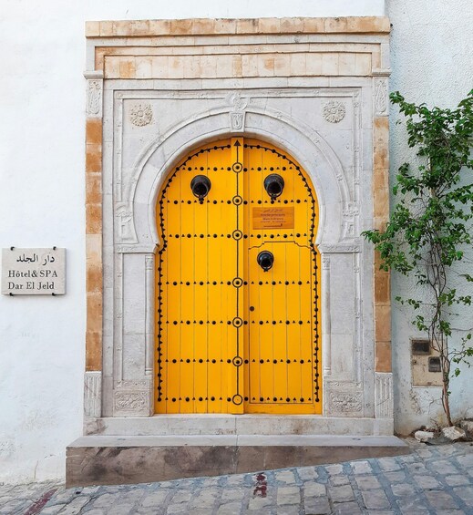 A bright yellow door with black decorative elements, a plaque reading 'Entrée principale,' and a sign for 'Hotel & SPA Dar El Jeld.' 5