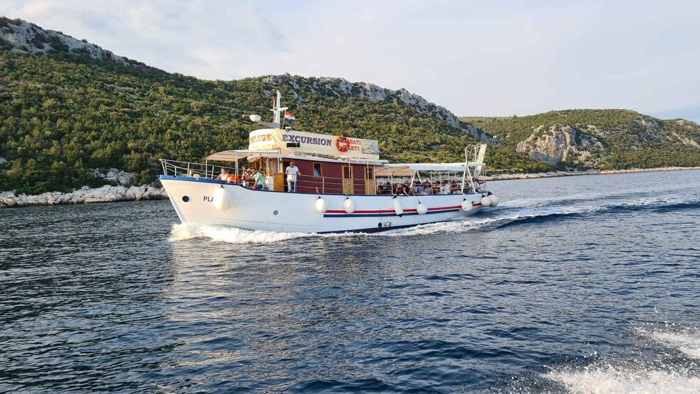 A white boat with 'EXCURSION' written on the side, moving on a body of water with a mountainous backdrop. 1