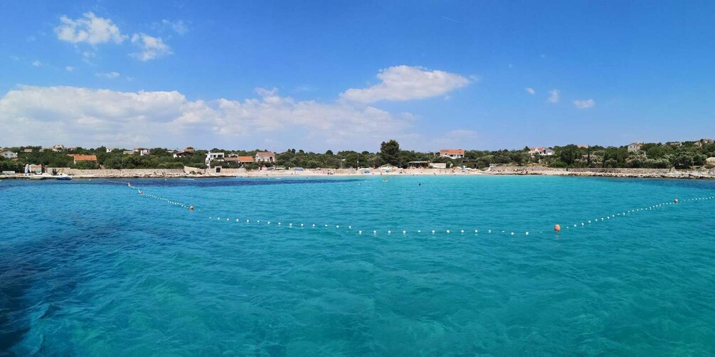 A coastal area with clear turquoise waters, a beach, and buildings in the background. 2