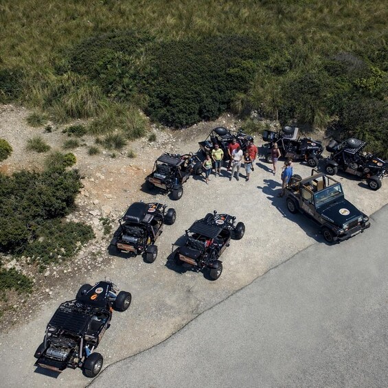 An aerial view of a group of off-road vehicles parked on a dirt road with people standing around them. 5