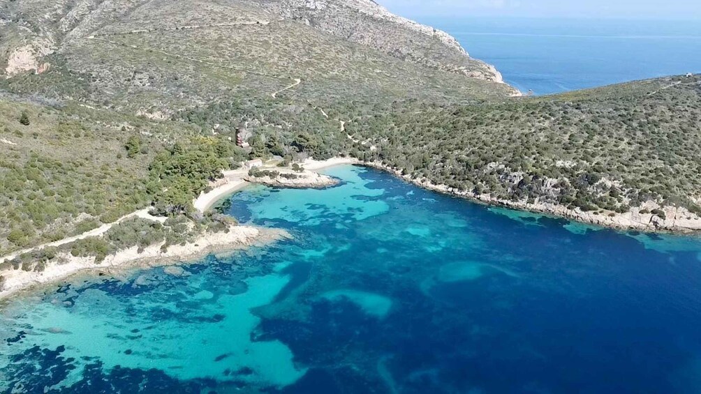 A coastal landscape with a clear blue sea, a winding road, and a small settlement surrounded by greenery. 5