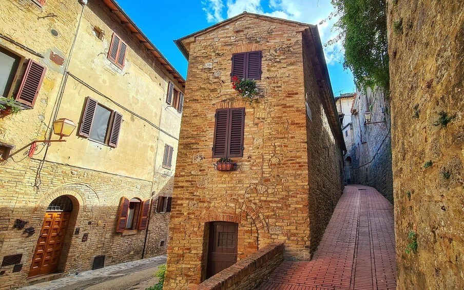 A narrow street flanked by historic stone buildings with arched doorways and wooden shutters. 5
