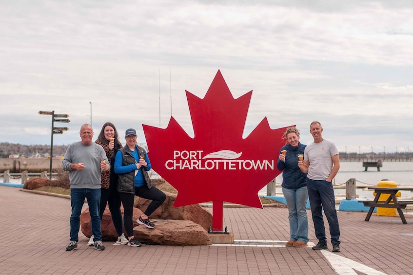 A group of people standing in front of a large red maple leaf sign with 'Port Charlottetown' written on it. 4