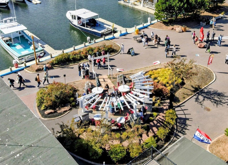 A riverside park with a circular seating area, boats docked nearby, and people walking around. 2