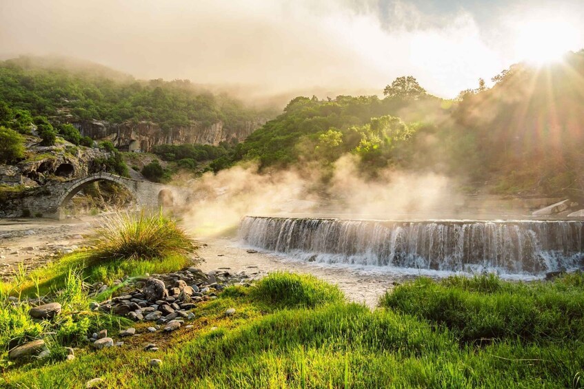 A waterfall, a stone bridge, and lush greenery. 1