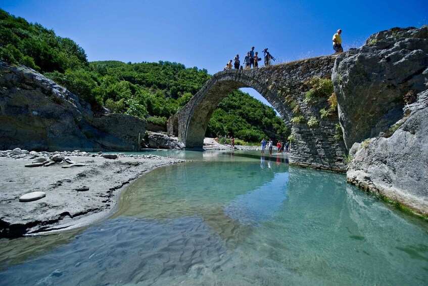 A stone bridge over a clear river, surrounded by lush greenery. 3