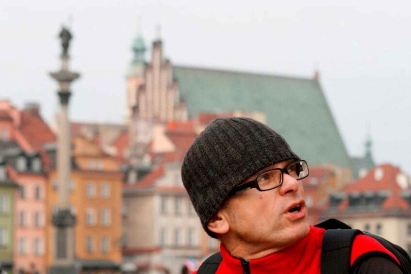 A person wearing a red jacket and a beanie, standing outdoors with buildings in the background. 2