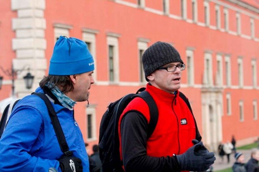 Two people in winter clothing, one in a blue jacket and the other in a red jacket, standing in front of a red building with white windows. 3