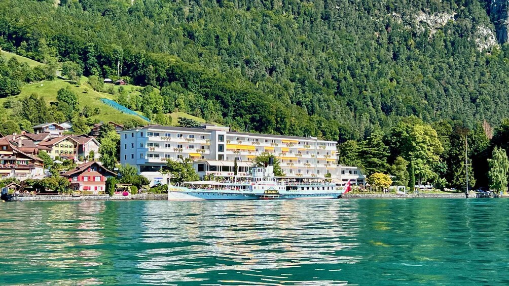 A lake with a boat and a hotel building surrounded by forested hills. 3