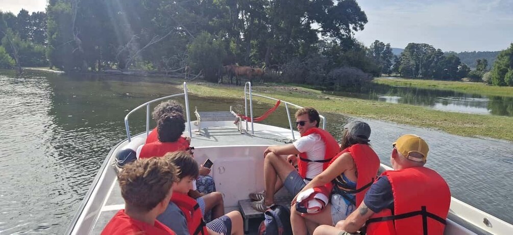 A group of people on a boat with life jackets, surrounded by calm water and greenery. 4