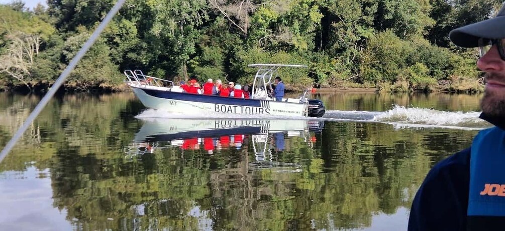 A boat named 'BOATTOURS' with passengers and a guide on a calm river surrounded by greenery. 5