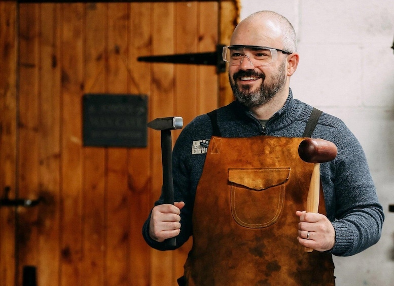 A person holding a hammer and a mallet, wearing a brown apron, with a wooden door and a sign in the background. 3