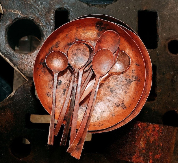 A rusty metal plate with several spoons and a ladle. 4