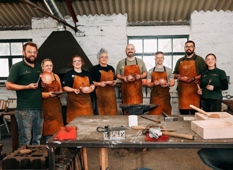 A group of people in a workshop holding pottery items, with an anvil and tools on a workbench. 1