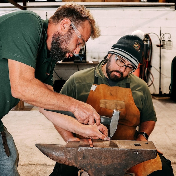 Two individuals working with a hammer and an anvil in a workshop. 5