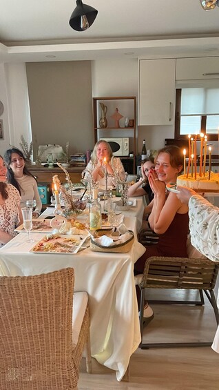 A group of people seated at a dinner table with lit candles, plates of food, and a bottle of wine. 1