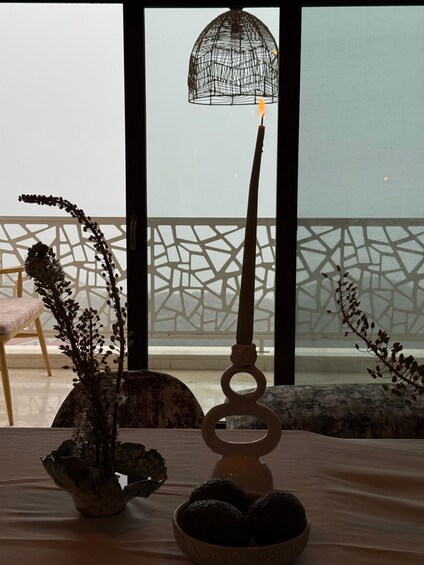 A table with a candle, a decorative plant, and a bowl of fruits. 5