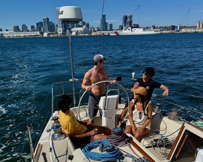 A sailboat with three people on board, a city skyline in the background, and calm waters. 2