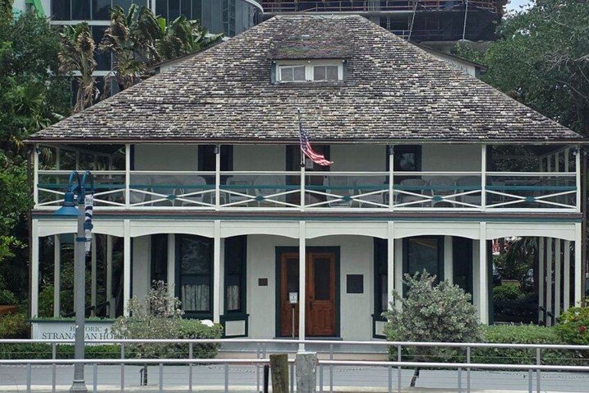 A two-story house with a balcony, a flag, and a sign that reads 'Strand Sanitary Hotel.' 3