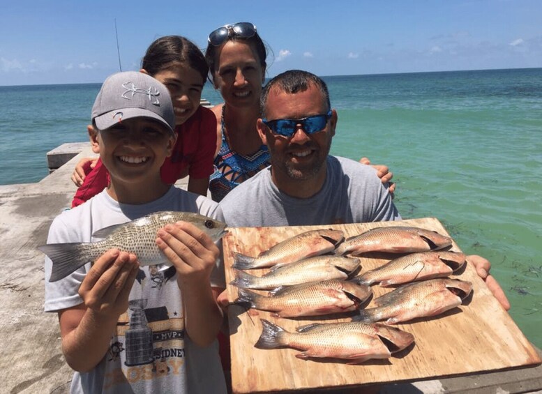 A group of people holding fish on a wooden board by a body of water. 1