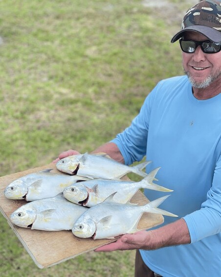 A person holding a wooden board with several fish. 2