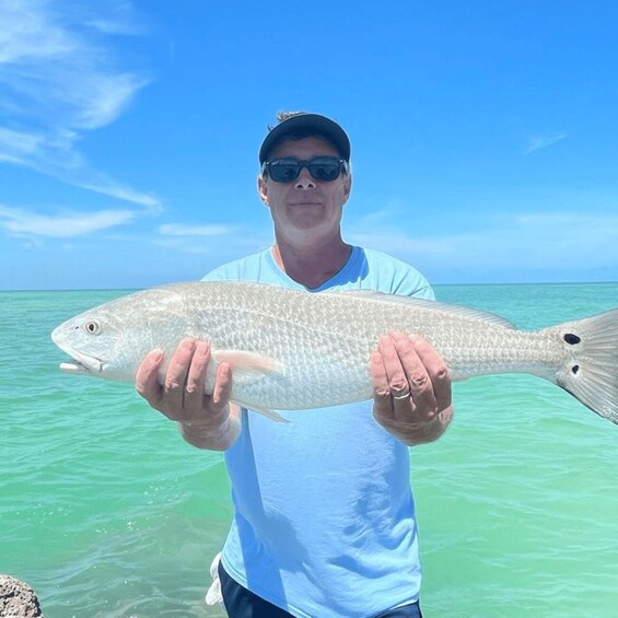 A person holding a fish by the water. 3