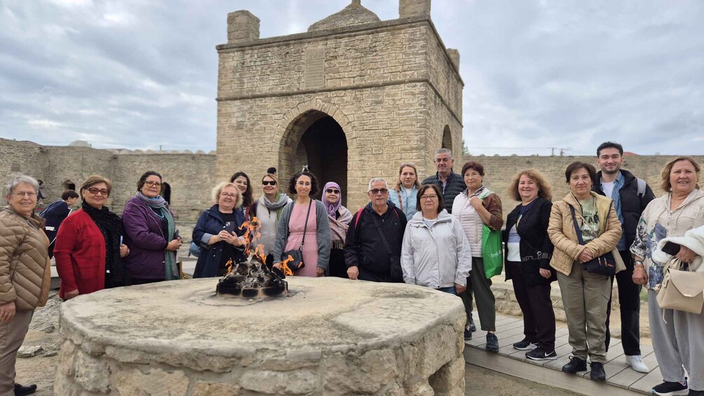 A group of people gathered around a stone structure with a fire in the center, set against a cloudy sky. 3