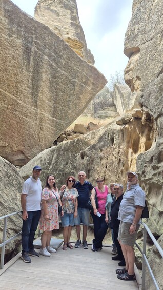 A group of people standing on a wooden platform in a rocky canyon with large boulders and a clear sky. 5