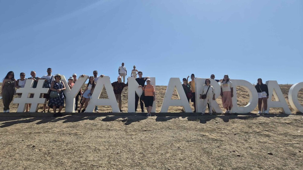 A group of people standing in front of large white letters spelling 'YAMANDAS' on a dry, rocky terrain. 4