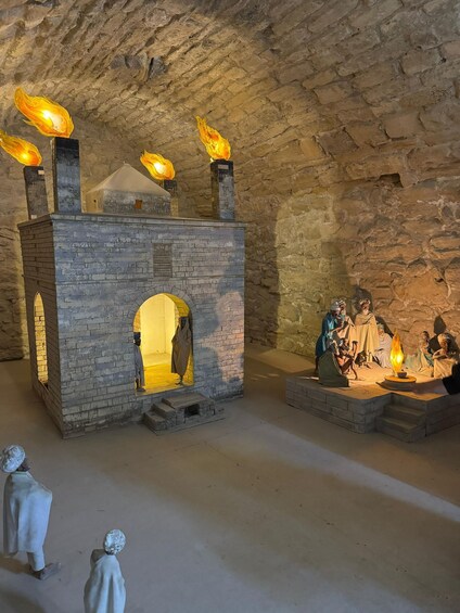 A stone building with a central arched doorway, a small balcony with a fire, and figures in period attire. 2