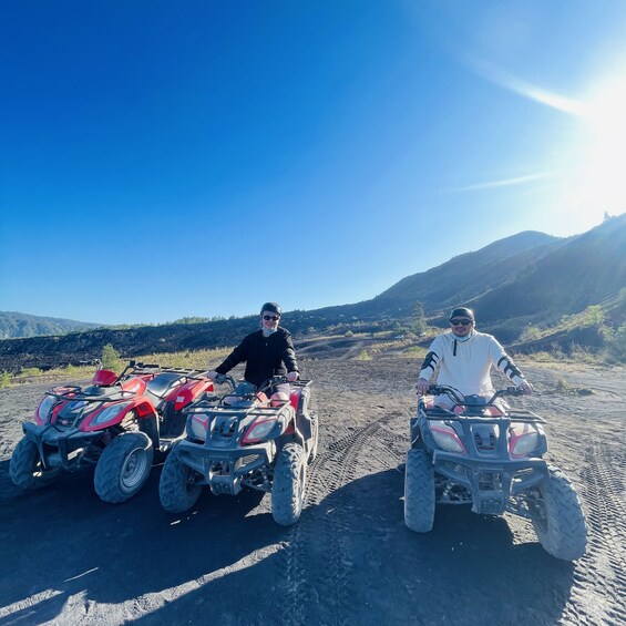 Two people on ATVs in a rocky terrain with mountains in the background. 4
