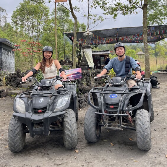 Two people on ATVs in a natural setting with trees and a building in the background. 3