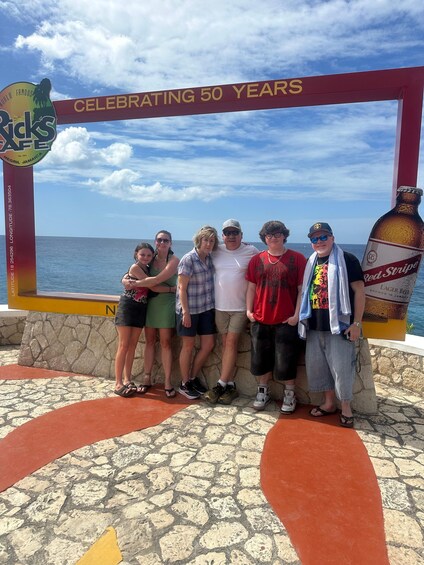 A group of people posing in front of a commemorative sign for 50 years, with a beach and ocean in the background. 4