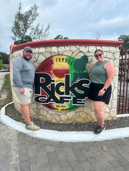 Two people standing in front of a sign for Rick's Famous Negril Jamaica. 3