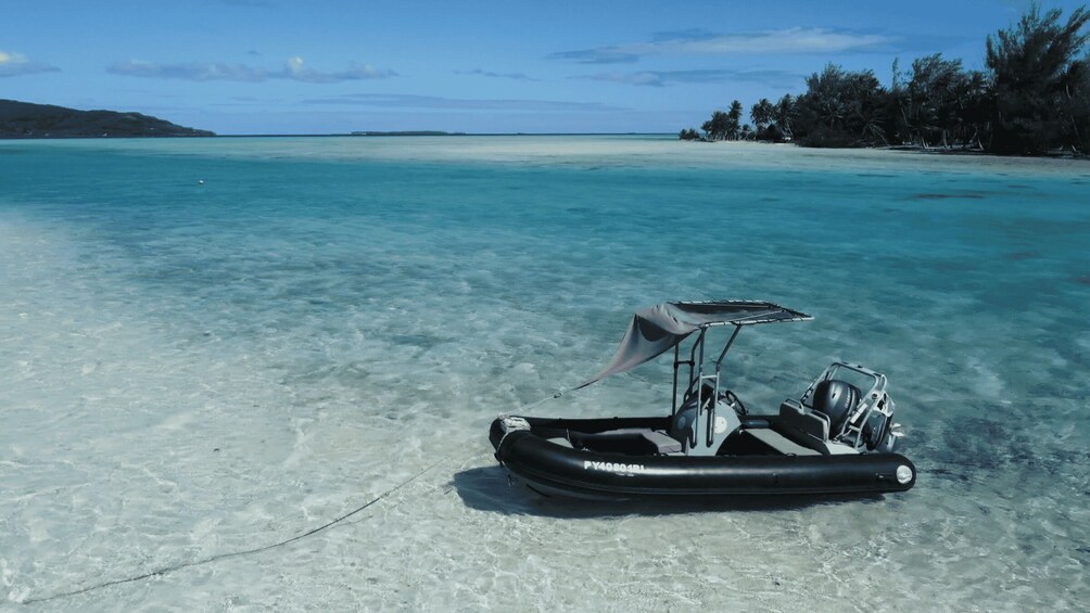 A clear turquoise sea with a small inflatable boat anchored on the sandy beach. 1