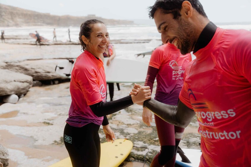 People in red and pink shirts holding surfboards on a rocky beach. 1