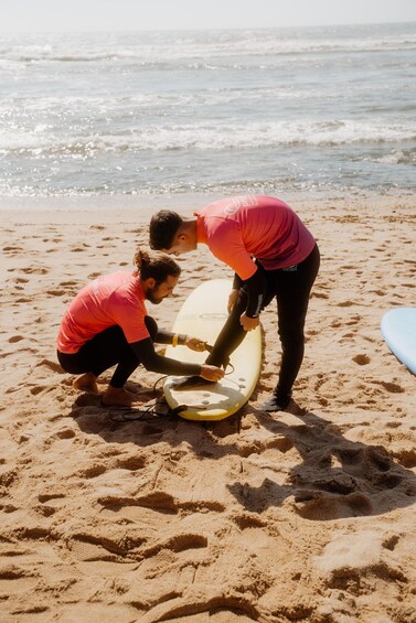 Two people on a beach with surfboards, one standing and one crouching, preparing to surf. 3